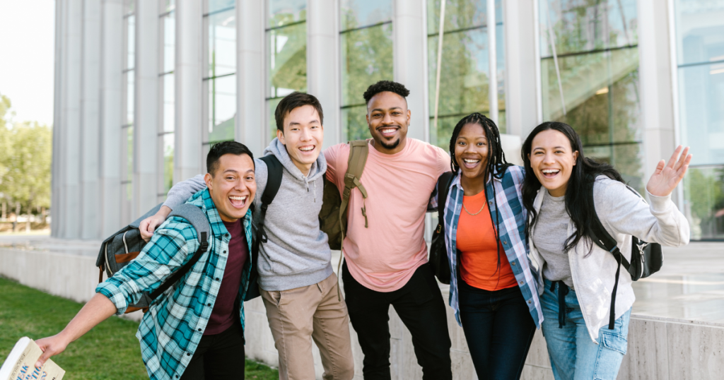 5 young adults smiling outside a school building.